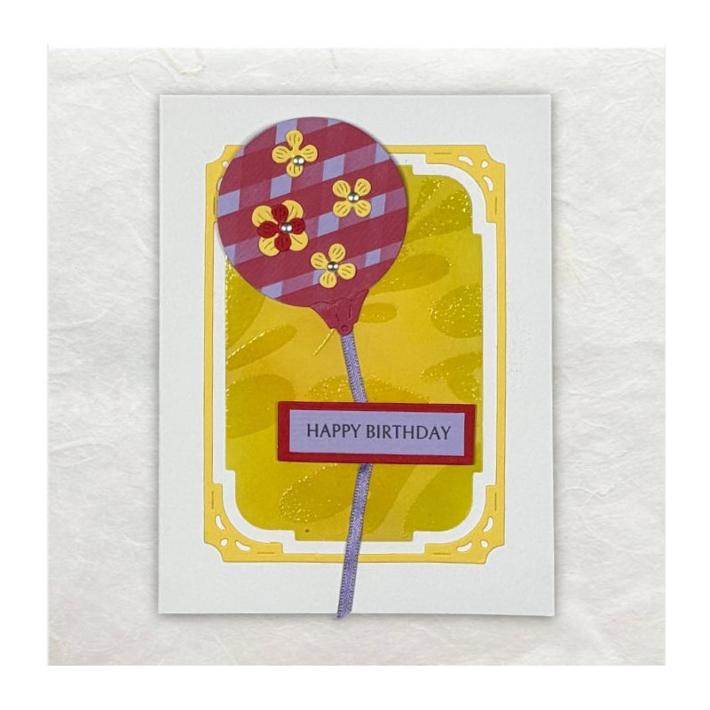 Een verjaardagsballon kronkelt zijn weg omhoog. Op de achtergrond glimmende bladertakken.